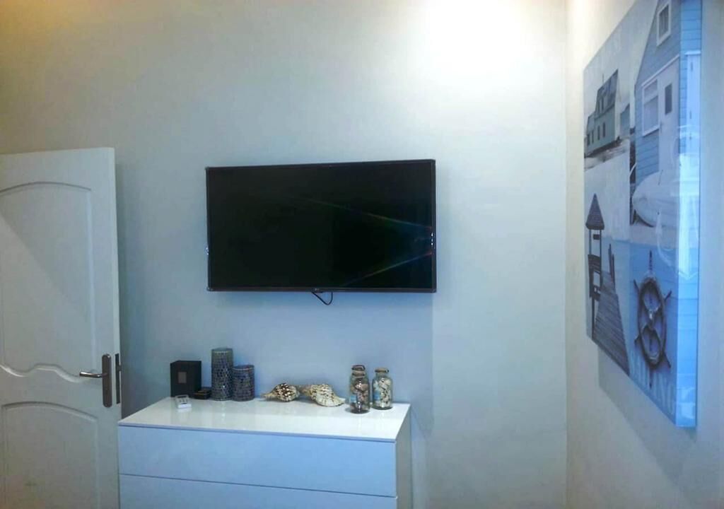 A room with a flat-screen TV mounted on the wall, a white console table with decorative items, and a framed picture on the wall.