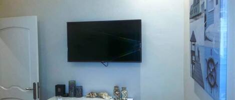 A room with a flat-screen TV mounted on the wall, a white console table with decorative items, and a framed picture on the wall.