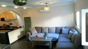 Een moderne woonkamer met een bank, een salontafel en een keukenhoek met kasten en een aanrecht.