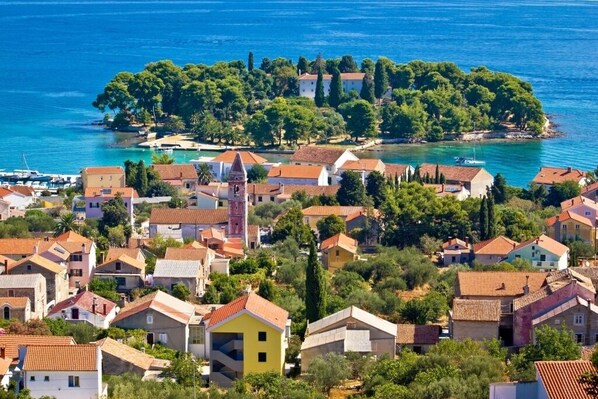 A coastal village with traditional Mediterranean architecture, a prominent church, and a small island with dense greenery.