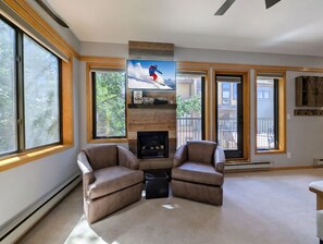 A living room with a fireplace, two armchairs, a television, and large windows. - Great Studio condo only steps from the Lifts! Hot Tubs and Fire Pit on site (Keystone)