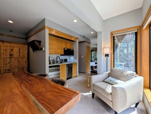 A spacious living area with a large wooden dining table, a sofa, and a view of a balcony. - Great Studio condo only steps from the Lifts! Hot Tubs and Fire Pit on site (Keystone)