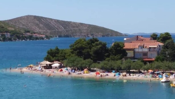 A coastal beach scene with a clear view of the sea, a sandy beach, and a building with a red roof. - Apartment in Grebaštica with Seaview, Terrace, Air condition, WIFI (886-2) (Grebaštica)