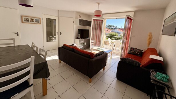 A modern living room with a dining area, a sofa, a TV, and a balcony with a view. - Agréable T3 en Duplex dans résidence avec piscine (091) (Biscarrosse)