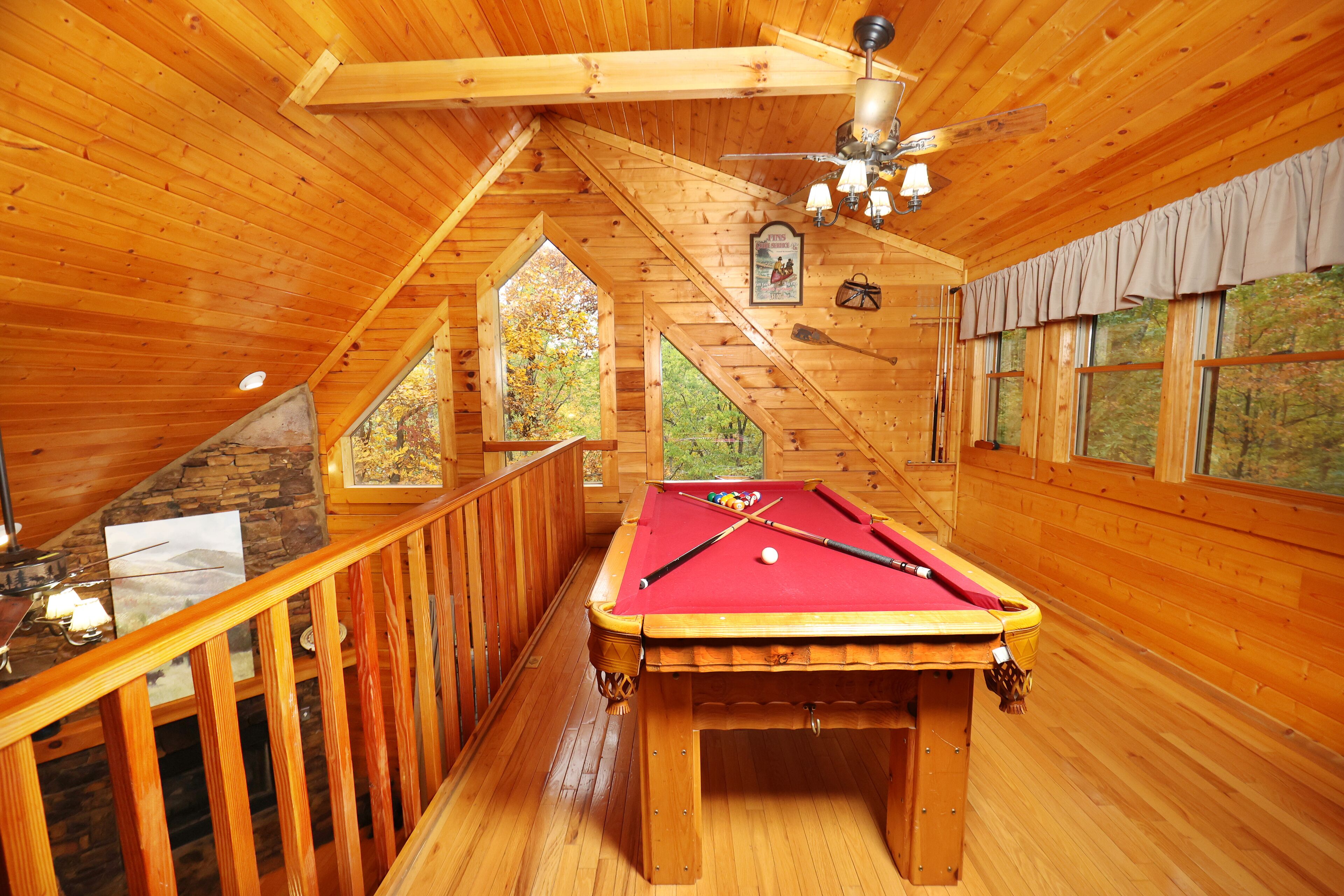Un intérieur en bois avec une table de billard, des rampes en bois et un ventilateur de plafond.