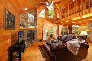 A log cabin interior with a fireplace, leather sofa, wooden walls, and a balcony. - Premier Cabin Private Location in the Mountains, FREE Access to Resort Amenities (Sevierville)