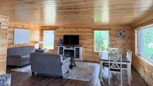 A wooden cabin interior with a sofa, TV, dining table, and chairs. - Veeder Lodge | West Twin Lake Retreat (Lewiston)