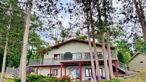 A two-story house with a balcony, a staircase, and a small shed in a wooded area. - Veeder Lodge | West Twin Lake Retreat (Lewiston)