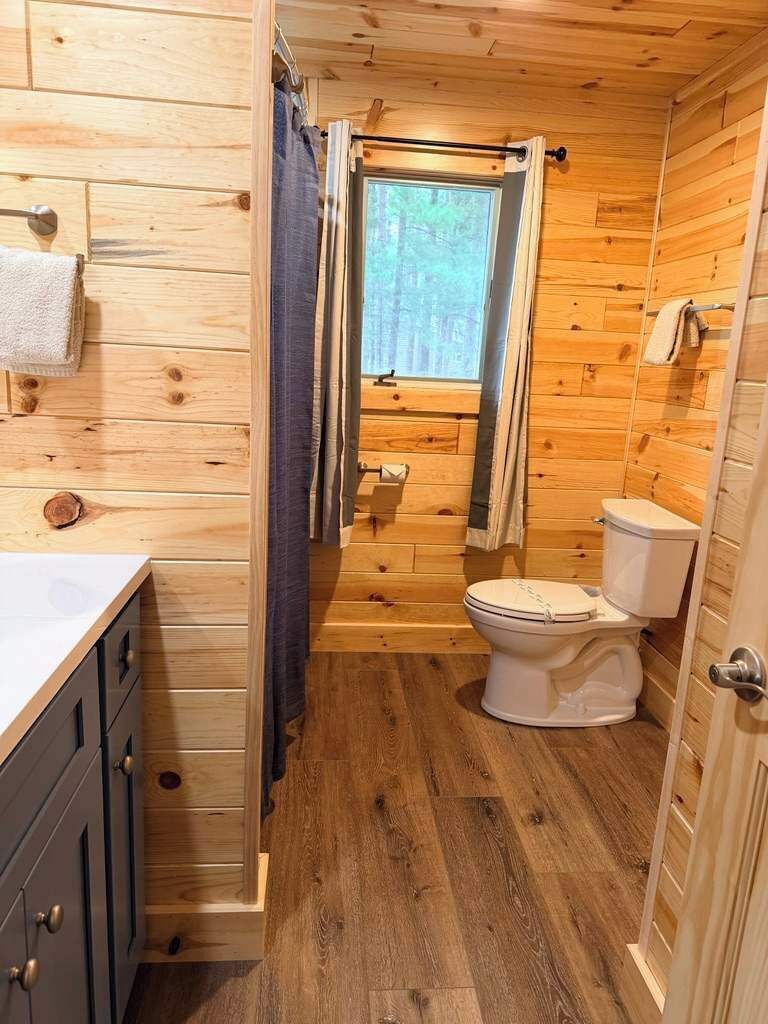 A wooden cabin bathroom with a toilet, a shower curtain, and a window.