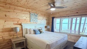 A wooden-paneled bedroom with a bed, bedside tables, and a window with a view. - Veeder Lodge | West Twin Lake Retreat (Lewiston)