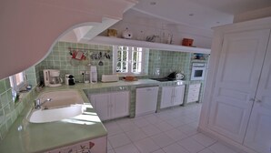 A kitchen with a sink, countertop, and cabinets. There is a window with a view of greenery outside. - Villa 10 people – Private infinity pool – Sea view – Wifi – Air conditioning – Sainte... (STE MAXIME)