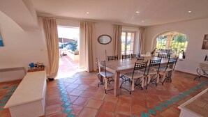 A dining area with a large table and chairs, a bench, and a view of the outdoors through large windows. - Villa 10 people – Private infinity pool – Sea view – Wifi – Air conditioning – Sainte... (STE MAXIME)