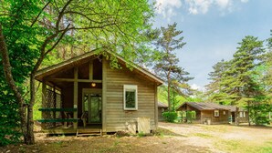 A rustic cabin with a porch, surrounded by trees.