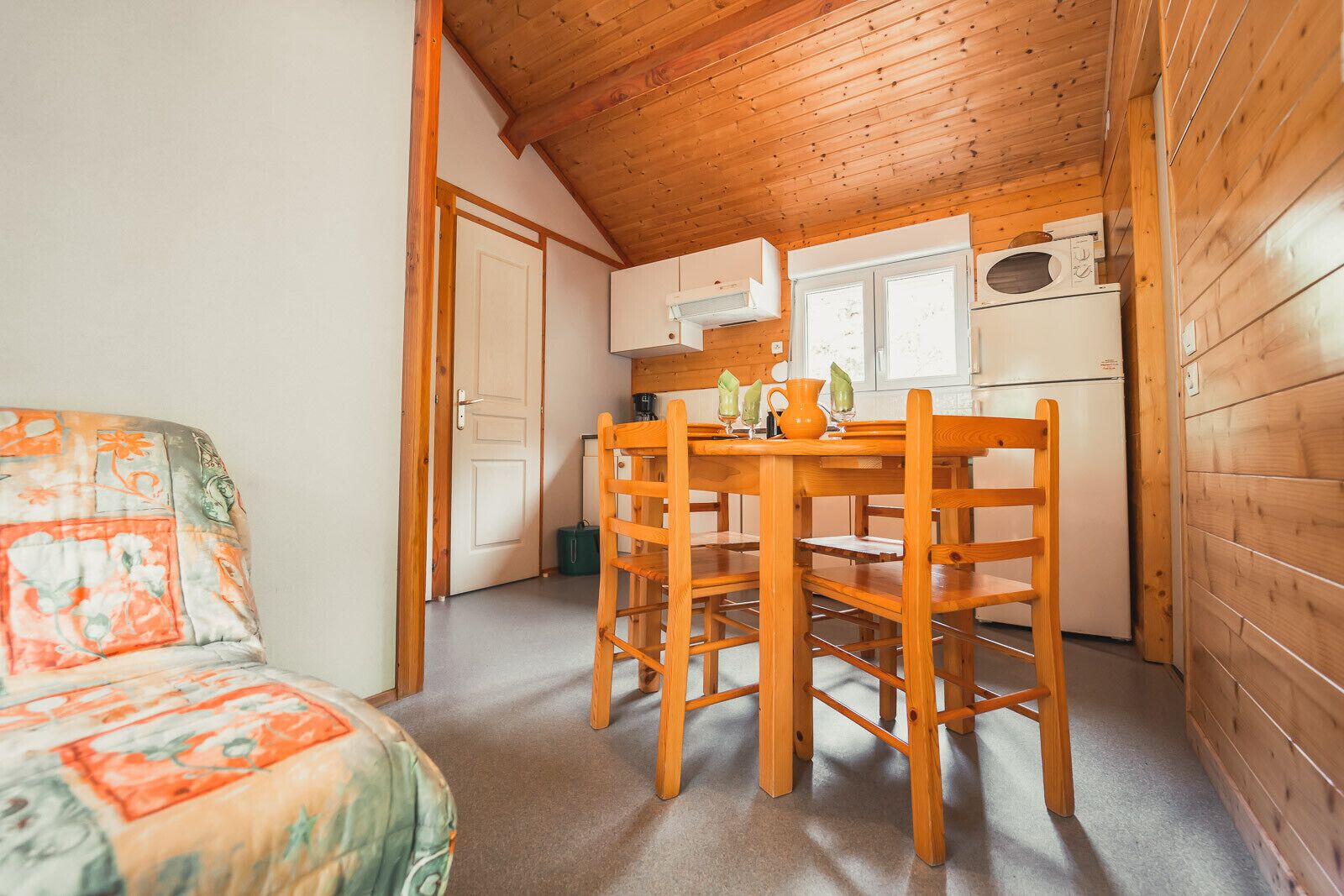 Una cabaña acogedora con interior de madera, una mesa de comedor con sillas, una zona de cocina con microondas y una puerta que da a otra habitación.