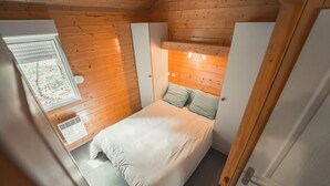 A bedroom with a wooden ceiling, a bed with white bedding, a window, and a door.