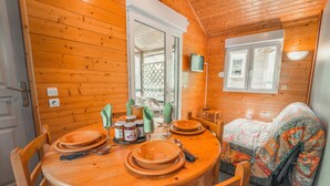 A cozy cabin interior with a wooden dining table set for four, a bed with a colorful blanket, and a window with a view of the outside.
