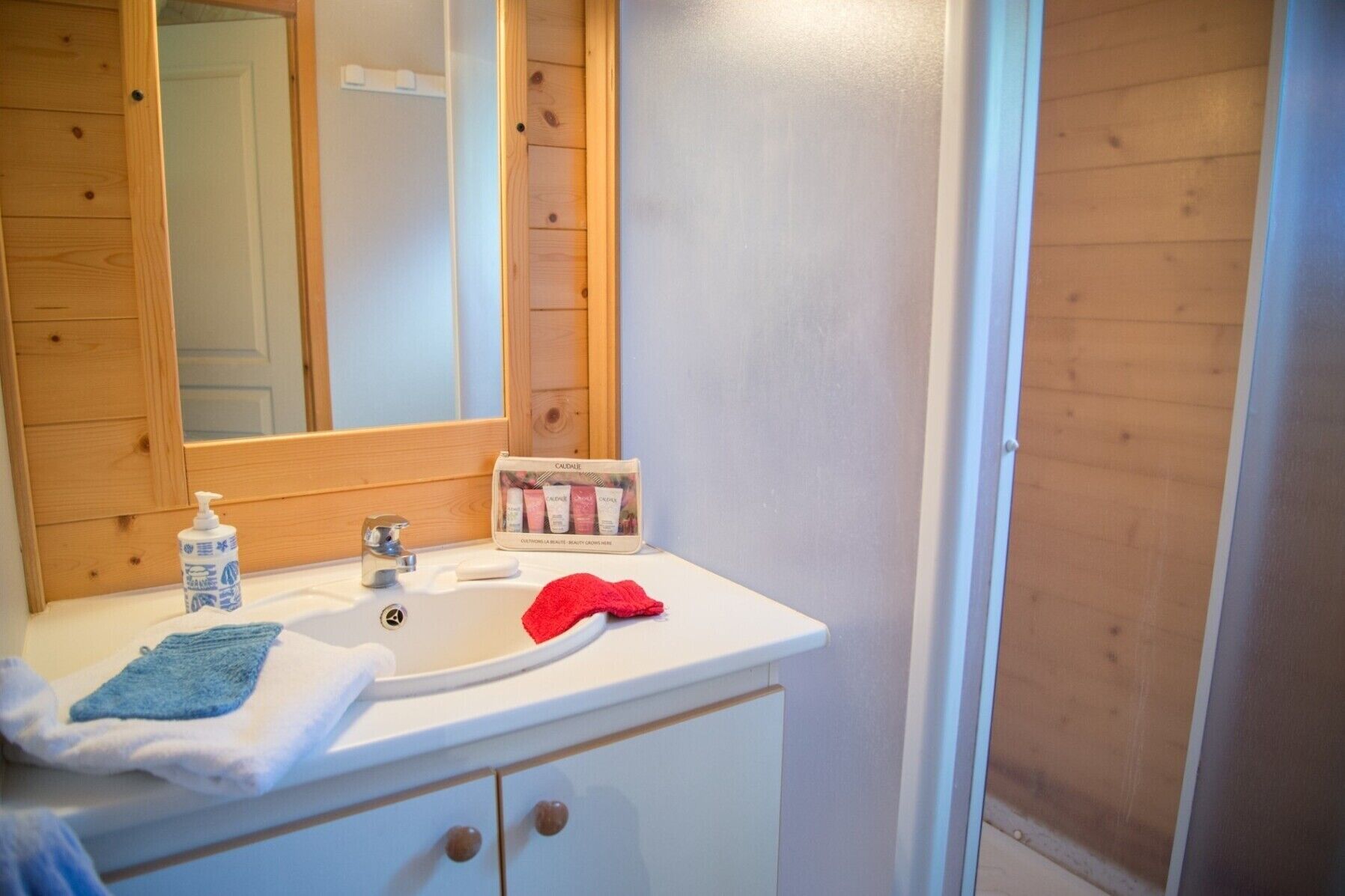Un baño con tocador de madera, un espejo, un lavabo, una toalla roja y una botella de loción.