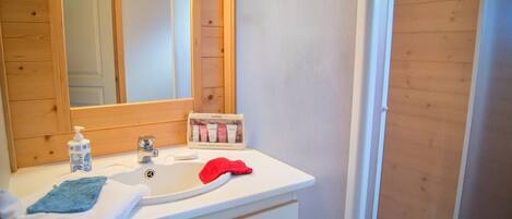 Un baño con tocador de madera, un espejo, un lavabo, una toalla roja y una botella de loción.