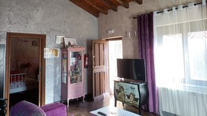 A living room with a wooden ceiling, a pink cabinet, a television, and a window with purple curtains. - Mudayyan house for couples or small families. (Coca de Alba)