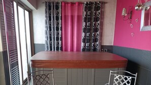 A room with a wooden bar, two metal chairs with pink cushions, a small table with a tray of decorative items, and a window with multiple curtains. - Mudayyan house for couples or small families. (Coca de Alba)