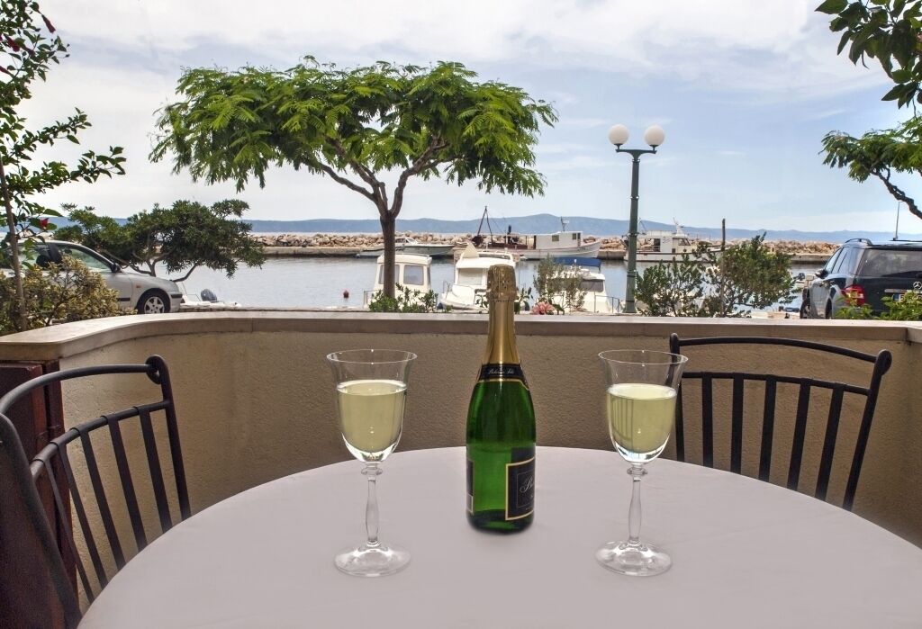 A table with a bottle of champagne and two glasses on a balcony overlooking a marina with boats and a body of water.