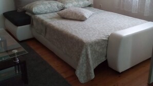 Makuuhuoneessa on sänky, yöpöytä, tuoli, ikkuna, jossa on verhot, ja seinällä on taulu.