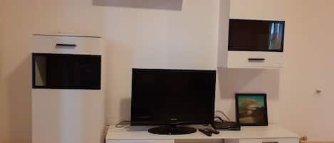 A modern living room with a flat-screen TV, a large TV, and a white entertainment unit with drawers.