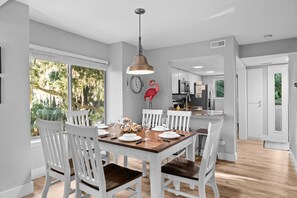 Un comedor con una mesa de madera y sillas blancas, una lámpara colgante y vistas al exterior.