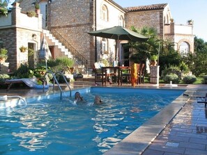 A swimming pool with a stone building in the background, a covered seating area, and a staircase leading to the building.