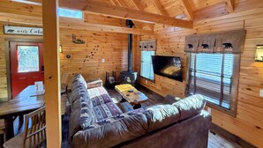 A cabin interior with a wooden ceiling, a sofa with patterned cushions, a television, and a fireplace. - BC Log cabin 1 mile from Mt Washington Hotel, beach, slope views! Hot tub, volleyball, trails! (Bretton Woods)