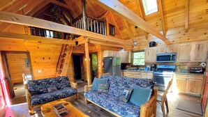A cozy cabin interior with a wooden floor, a sofa set, a dining table, and a kitchen area. - BC Log cabin 1 mile from Mt Washington Hotel, beach, slope views! Hot tub, volleyball, trails! (Bretton Woods)