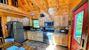 A wooden cabin kitchen with a refrigerator, stove, microwave, and wooden cabinets. - BC Log cabin 1 mile from Mt Washington Hotel, beach, slope views! Hot tub, volleyball, trails! (Bretton Woods)