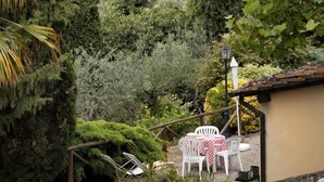 A garden with a table and chairs, a lamp post, and a view of a hill with buildings.