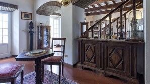 A traditional interior with a wooden staircase, a dining table with chairs, and a cabinet with decorative items.