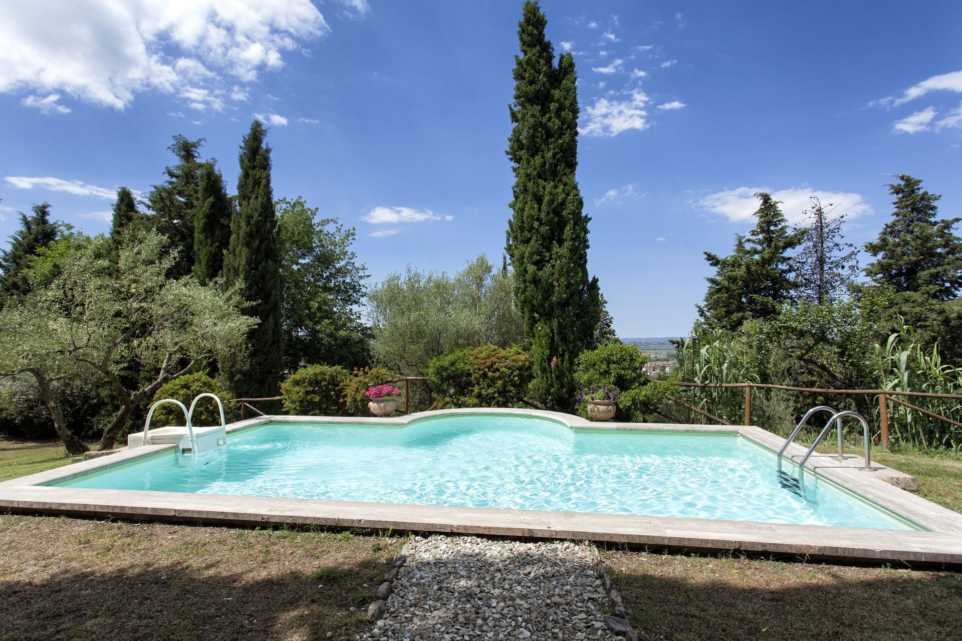 A rectangular swimming pool with a clear blue water surface, surrounded by a grassy area and various trees.