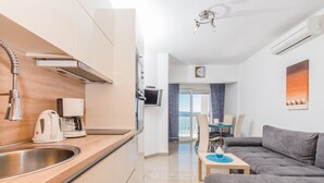 A modern kitchen with a built-in oven, a coffee machine, and a sink. There is a gray sofa and a dining table with chairs in the living area. - Apartment in Crikvenica with Seaview, Terrace, Air condition, WIFI (3492-2) (Crikvenica)