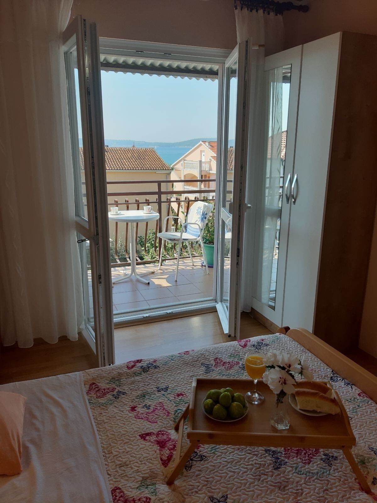 A bedroom with a bed, a tray with fruit and a glass of juice, and a balcony with a table and chairs.