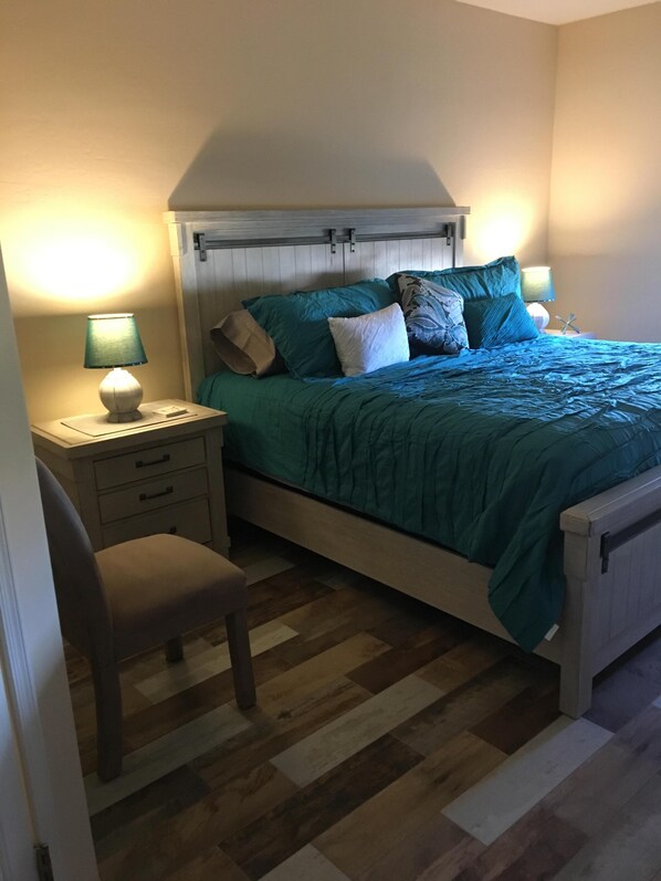 A bedroom with a bed, nightstands, a chair, and a wooden floor.