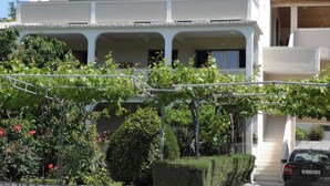 A two-story house with a balcony, a car parked in front, and a garden with grapevines and bushes. - Apartment in Lopar with Terrace, Air condition, WIFI, Washing machine (893-3) (Lopar)