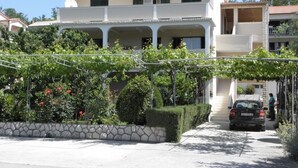 A two-story building with a tiled roof, a covered porch, and a car parked in the driveway. - Apartment in Lopar with Terrace, Air condition, WIFI, Washing machine (893-3) (Lopar)