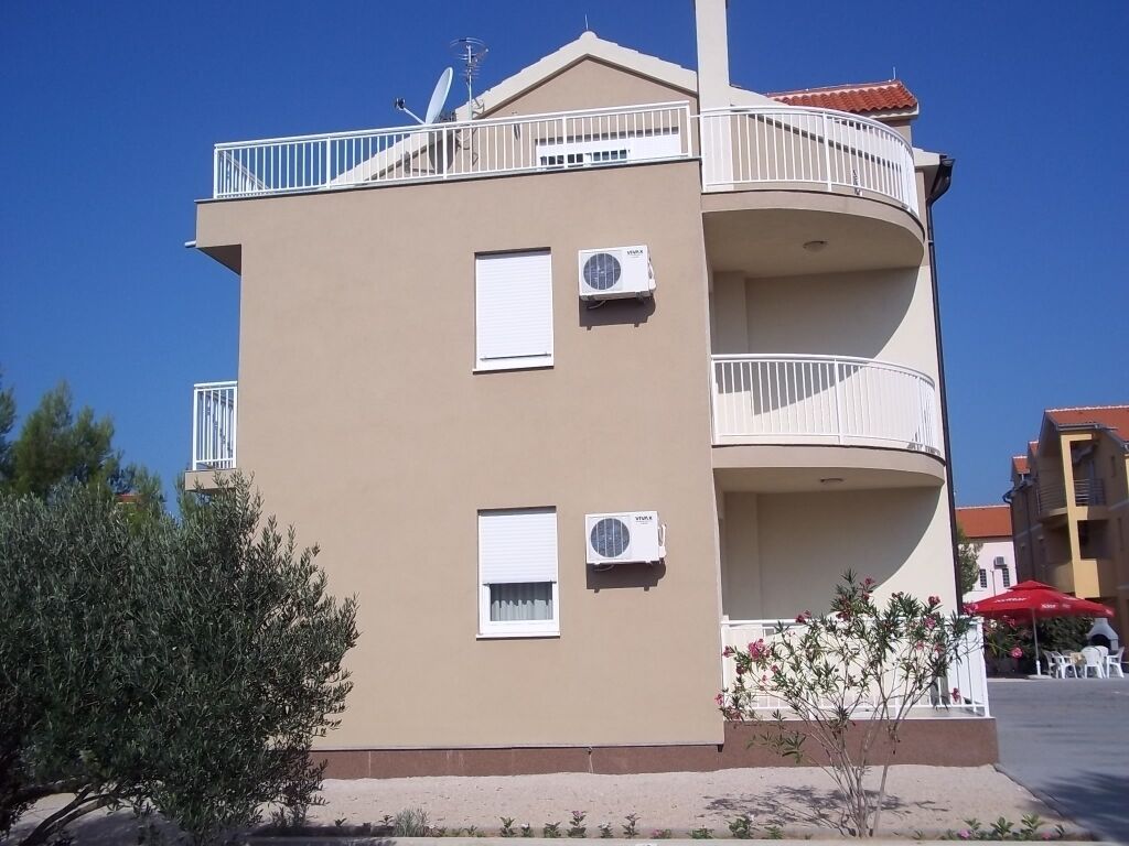 A multi-story building with balconies, air conditioning units, and a red umbrella in the background.