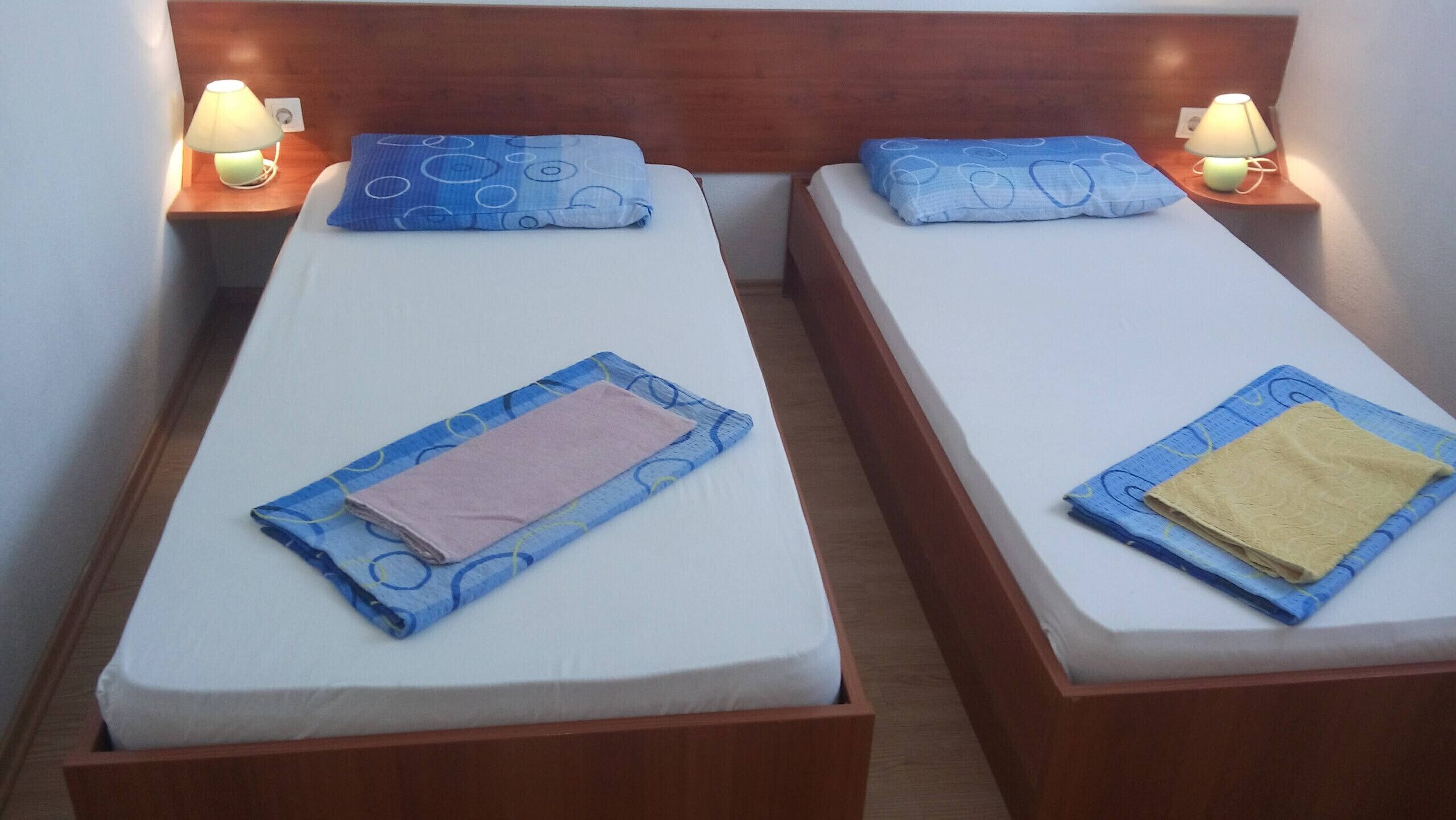 Dos camas individuales con cabeceros de madera, cada una con una mesita de noche y una lámpara.