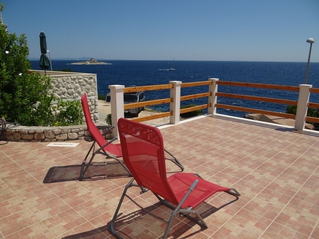 Una silla roja en un patio empedrado con vistas al mar y una barandilla de madera.