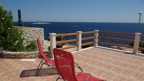 Une chaise rouge sur une terrasse carrelée donnant sur la mer, avec une balustrade en bois.