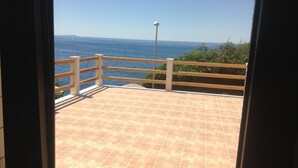 Une vue depuis un balcon doté d’un sol carrelé et d’une balustrade en bois, donnant sur une étendue d’eau et sur une terre lointaine.