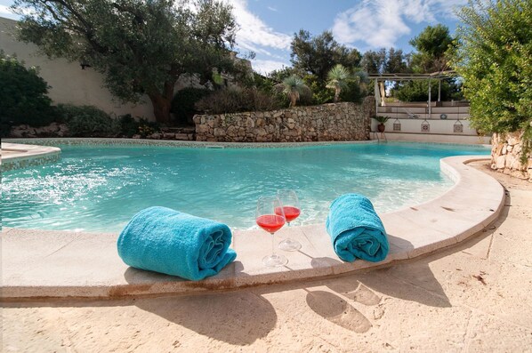 A pool area with two blue towels and two glasses of red liquid, likely wine, on a stone ledge.