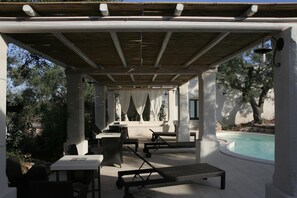 An outdoor patio with tables and chairs, a pool, and a pergola structure.