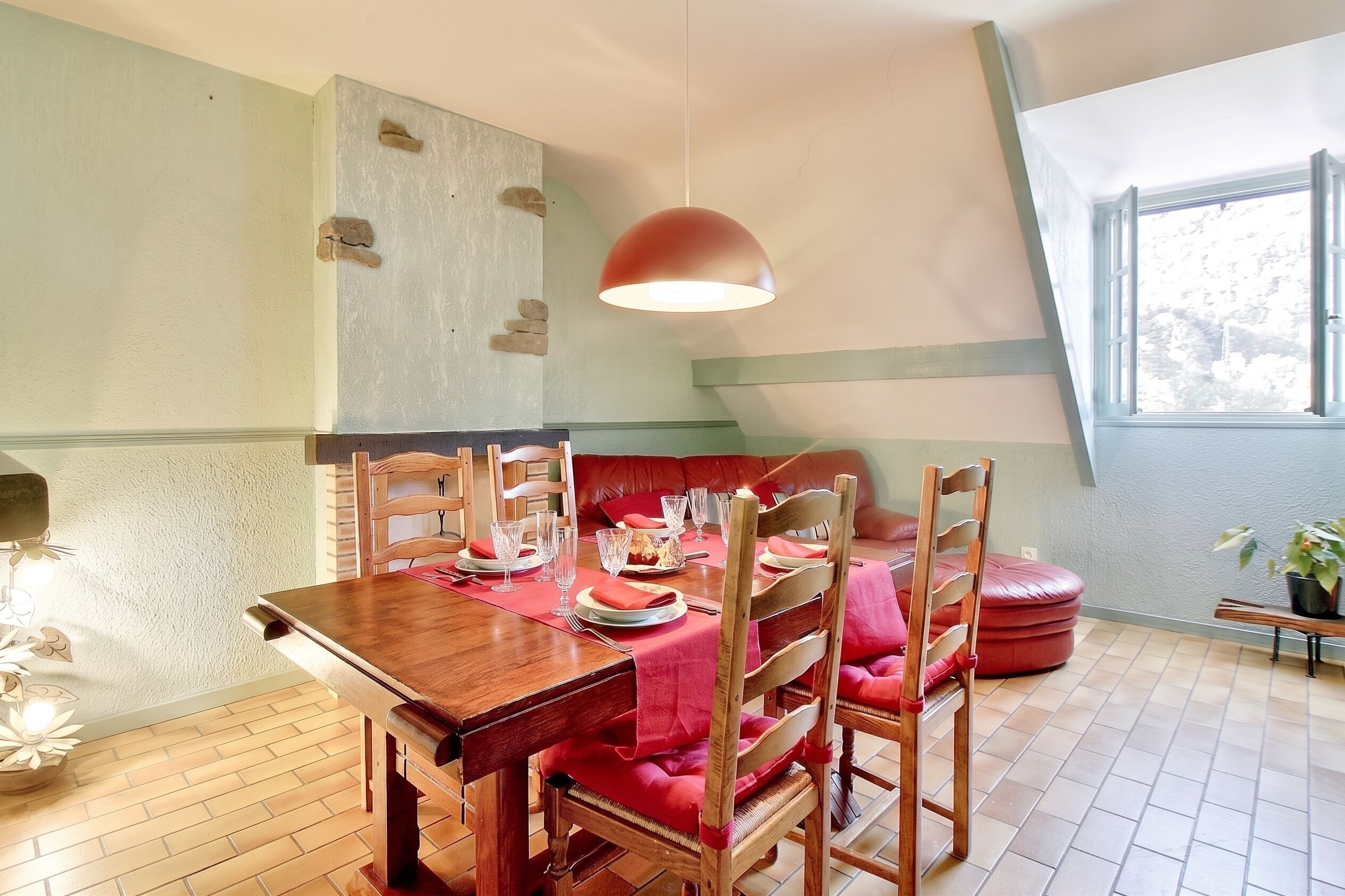Un coin repas avec une table en bois dressée pour quatre personnes, un banc rouge avec un coussin et une suspension.