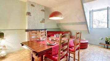 Un coin repas avec une table en bois dressée pour quatre personnes, un banc rouge avec un coussin et une suspension.