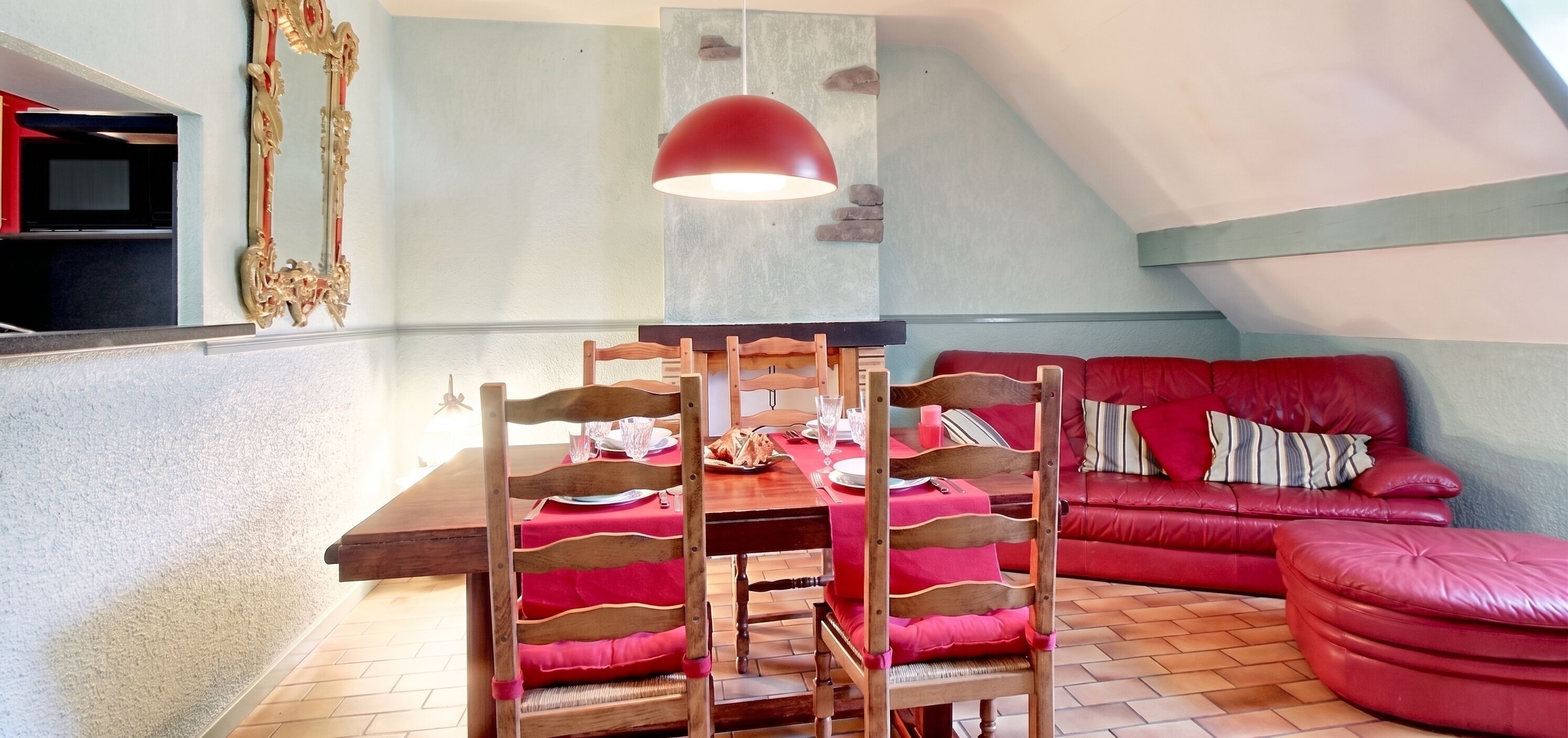 A dining area with a wooden table set for four, a red sofa, and a red pendant light.